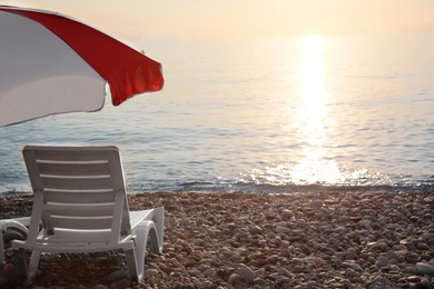 Photo of Empty sunbed and umbrella on stone beach near sea at sunset