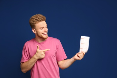 Photo of Portrait of happy young man with lottery ticket on blue background