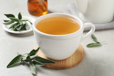 Photo of Cup of aromatic sage tea and fresh leaves on light grey table