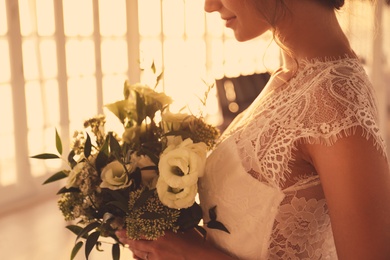 Photo of Bride in beautiful wedding dress with bouquet indoors, closeup