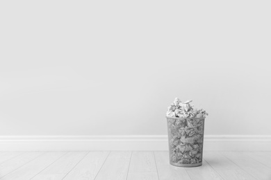 Photo of Metal bin and crumpled paper against light wall, space for text