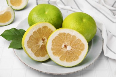 Photo of Whole and cut sweetie fruits with green leaves on white tiled table