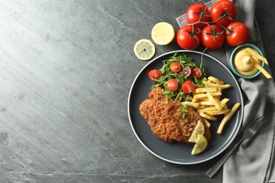 Photo of Tasty schnitzels served with potato fries, tomatoes and arugula on grey table, flat lay. Space for text