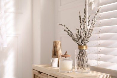 Photo of Glass vase with pussy willow tree branches and candle near window in room, space for text