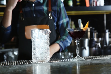 Photo of Barman with alcoholic cocktail and mixing glass of ice at counter in pub