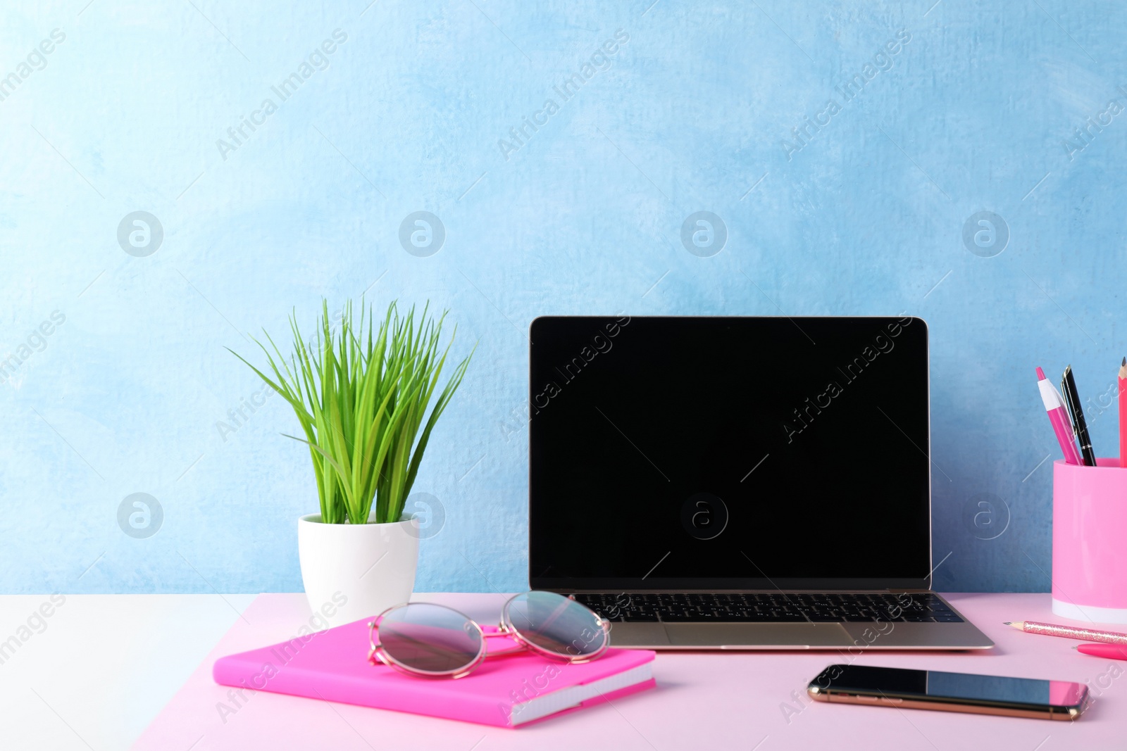 Photo of Comfortable workplace with modern laptop and plant near light blue wall. Space for design