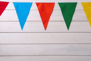 Photo of Bunting with colorful triangular flags on white wooden background. Space for text