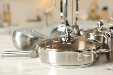 Photo of Set of shiny cooking utensils on white table against blurred background