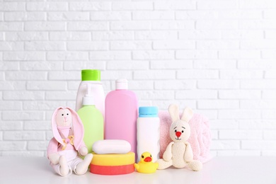 Photo of Baby accessories on table near white brick wall. Space for text