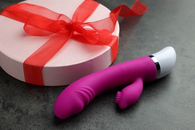Photo of Gift box and pink vaginal vibrator on grey table, closeup. Sex toy