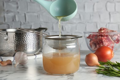 Photo of Straining delicious broth through sieve on white marble table