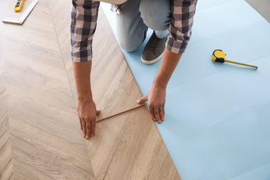 Photo of Worker installing laminated wooden floor indoors, closeup