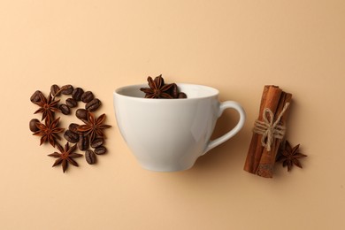 Photo of Cup with coffee beans, anise stars and cinnamon sticks on beige background, flat lay