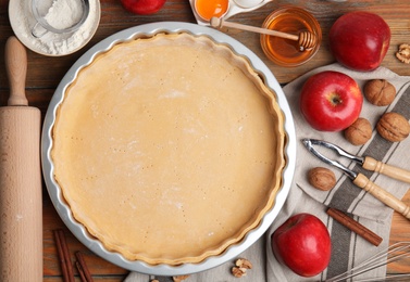 Photo of Raw dough and ingredients for traditional English apple pie on wooden table, flat lay