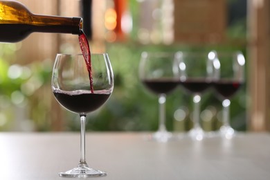 Photo of Pouring red wine from bottle into glass on table against blurred background, space for text