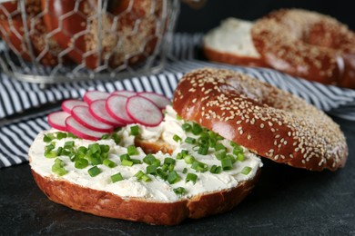 Photo of Delicious bagel with cream cheese, radish and green onion on black table, closeup