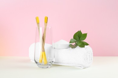 Photo of Bamboo toothbrushes, towel and bowl of baking soda on beige table against pink background