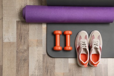 Photo of Dumbbells, sneakers and mats on wooden floor, flat lay. Space for text