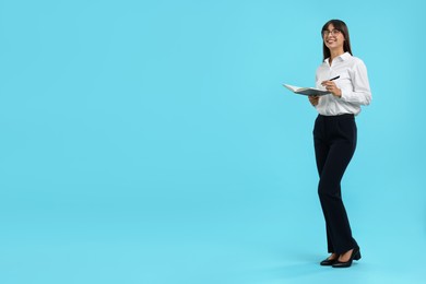 Photo of Happy secretary with notebook and pen on light blue background. Space for text