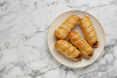 Photo of Delicious sausage rolls on white marble table, top view. Space for text