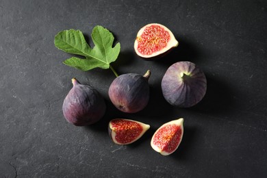 Photo of Fresh ripe figs and green leaf on black table, flat lay