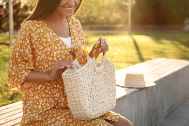 Photo of Young woman with stylish straw bag in park, closeup