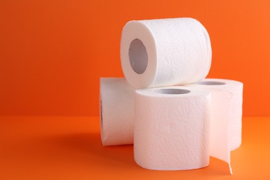 Photo of Soft toilet paper rolls on orange background, closeup. Space for text