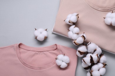 Photo of Cotton branch with fluffy flowers and t-shirts on light gray background, flat lay