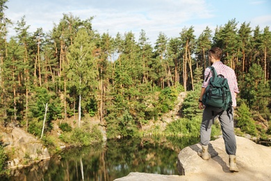 Photo of Young man on rock near lake and forest. Camping season