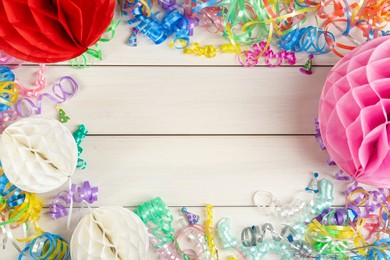 Photo of Frame of colorful serpentine streamers and other party accessories on white wooden table, flat lay. Space for text
