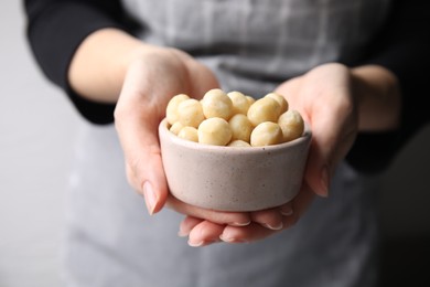 Photo of Woman holding bowl with delicious macadamia nuts, closeup