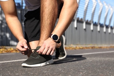 Photo of Sporty man tying shoelaces before running at stadium