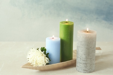 Photo of Candles with floral decor on table against color background