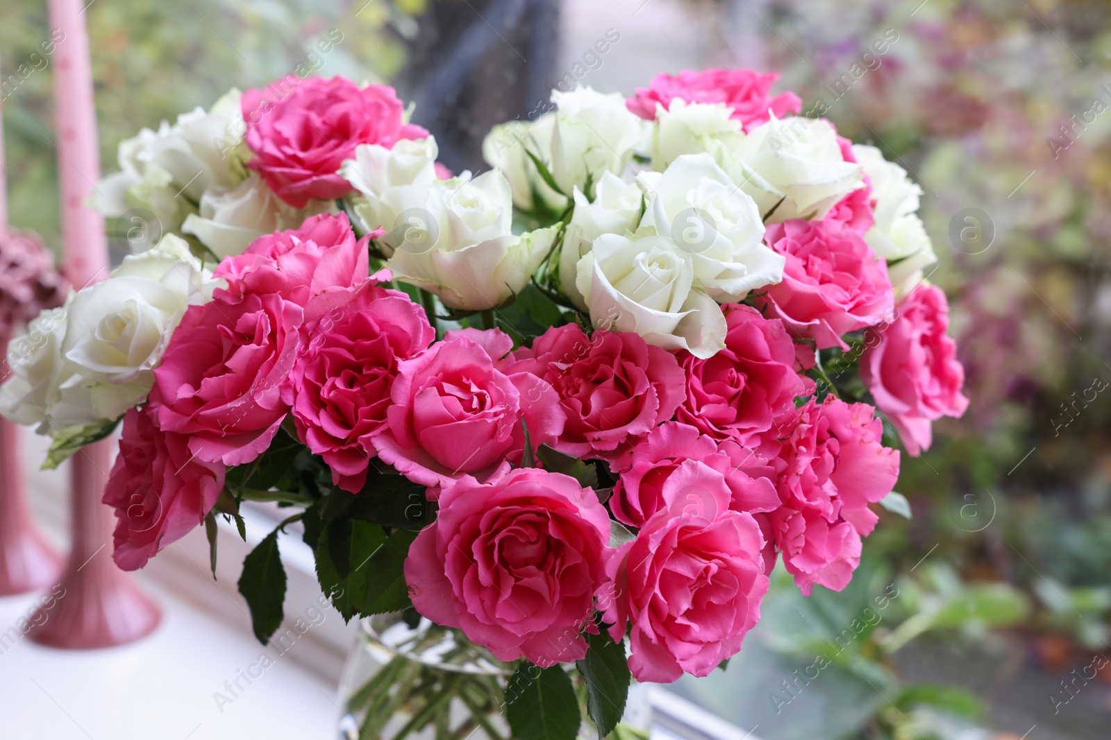 Photo of Vase with beautiful bouquet of roses and candles on windowsill indoors, closeup