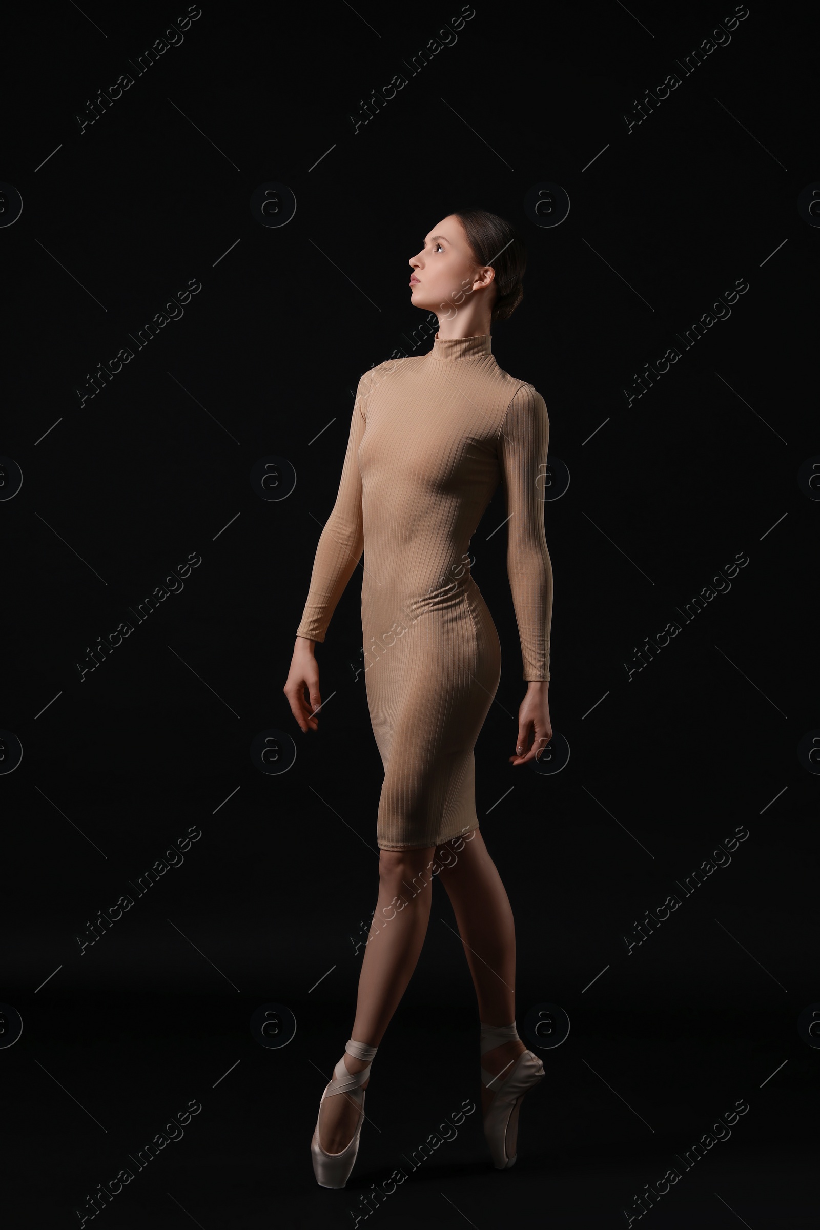 Photo of Young ballerina in pointe shoes dancing on black background