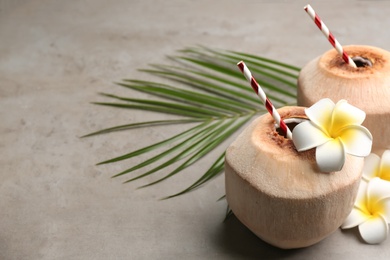Photo of Fresh coconuts with drinking straws and flowers on grey table. Space for text