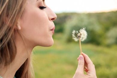 Photo of Attractive young woman blowing dandelion flower outdoors