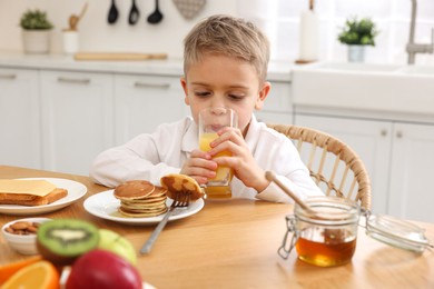 Photo of Breakfast time. Cute little boy drinking juice at table in kitchen