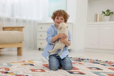 Photo of Little boy with cute puppy on carpet at home