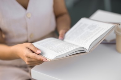 Photo of Woman reading book at white table outdoors, closeup