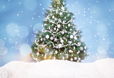 Image of Beautifully decorated Christmas tree and snow on light blue background. Bokeh effect