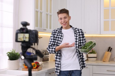 Photo of Smiling food blogger talking about spinach while recording video in kitchen