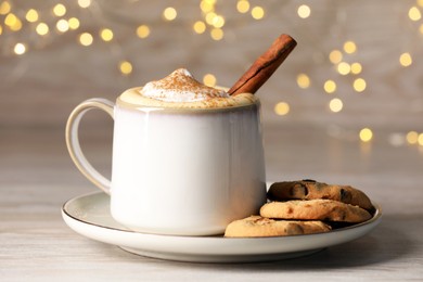 Photo of Cup of delicious eggnog with cinnamon and cookies on wooden table