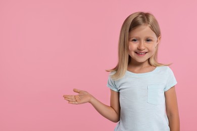 Photo of Special promotion. Little girl showing something on pink background. Space for text