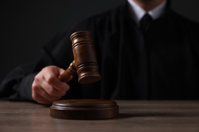 Photo of Judge with gavel sitting at wooden table against black background, closeup