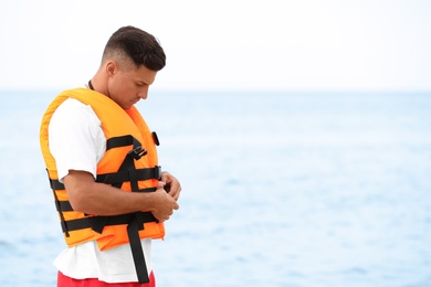 Photo of Handsome male lifeguard putting on life vest near sea
