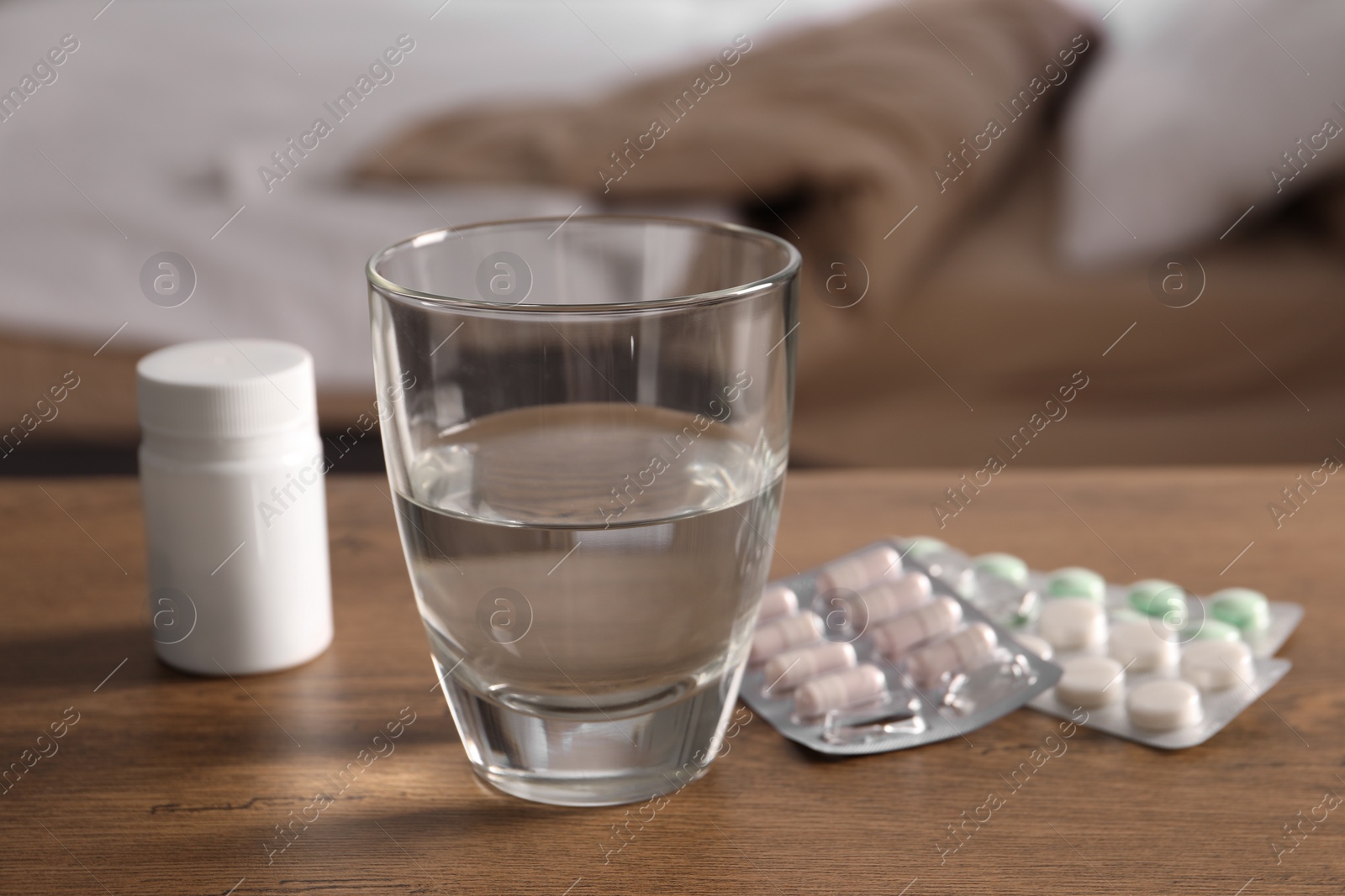 Photo of Glass of water, different pills in blisters and medical bottle on wooden table indoors