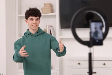 Photo of Smiling teenage blogger explaining something while streaming at home