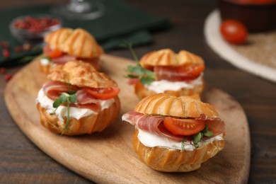 Photo of Delicious profiteroles with cream cheese, jamon and tomato on wooden table, closeup