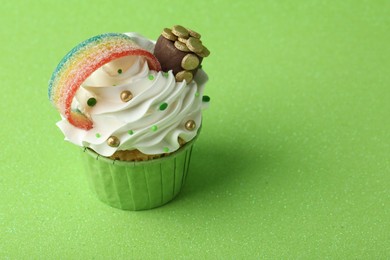 Photo of St. Patrick's day party. Tasty cupcake with sour rainbow belt and pot of gold toppers on green background. Space for text
